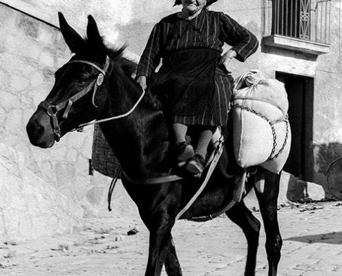Frau in Italien. 1967. © VG Bild-Kunst, Bonn 2026 Schwarz-Weiß-Fotografie von Pan Walther mit einer älteren Frau auf einem Esel in einer italienischen Ortschaft