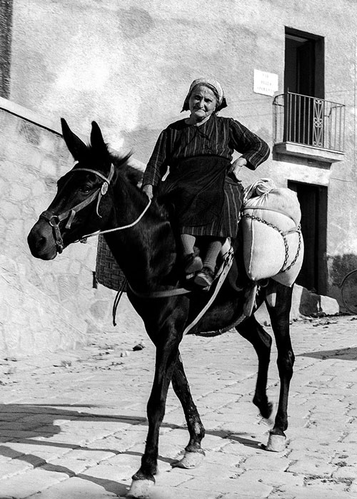 Frau in Italien. 1967. © VG Bild-Kunst, Bonn 2026 Schwarz-Weiß-Fotografie von Pan Walther mit einer älteren Frau auf einem Esel in einer italienischen Ortschaft