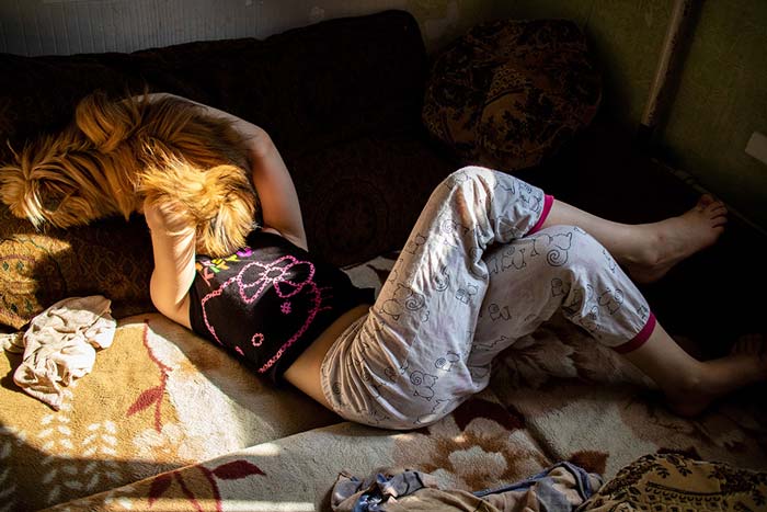 06_Versluis Fotografie „Nastya und Mila“ von Karine Zenja Versluis mit einem jungen Mädchen und einem Hund, die in einem von Sonnenlicht durchzogenen Innenraum auf einem Sofa liegen