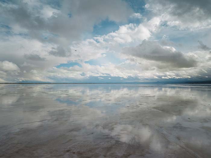 08.11.26–07.03.27<br>BOTTROP | Josef Albers Museum Quadrat Bottrop: Longing for Trust Fotografie „Near Highway 80“ von Trevor Paglen aus dem Jahr 2024: Eine weite, spiegelnde Wasserfläche reflektiert einen wolkenreichen Himmel. Am Horizont erstreckt sich eine schmale dunkle Landschaftslinie.
