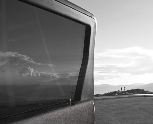 20.09.–06.12.26<br>LAER | Galerie Lengershaus: Fotografien von Aleš Sobota Schwarz-Weiß-Fotografie von Aleš Sobota mit dem Fenster und der Karosserie eines Fahrzeugs im Vordergrund sowie einer weiten Landschaft mit vereinzelten Personen am Horizont