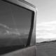 Schwarz-Weiß-Fotografie von Aleš Sobota mit dem Fenster und der Karosserie eines Fahrzeugs im Vordergrund sowie einer weiten Landschaft mit vereinzelten Personen am Horizont