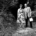 Schwarz-Weiß-Fotografie „Waldeslust (Im Wald)“ von Anna und Bernhard Blume aus den Jahren 1982/83: Das Künstlerpaar steht nebeneinander auf einem Waldweg. Anna Blume trägt ein geblümtes Kleid, Bernhard Blume ein kariertes Sakko und hält eine helle Tasche in der Hand.