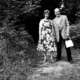 Schwarz-Weiß-Fotografie „Waldeslust (Im Wald)“ von Anna und Bernhard Blume aus den Jahren 1982/83: Das Künstlerpaar steht nebeneinander auf einem Waldweg. Anna Blume trägt ein geblümtes Kleid, Bernhard Blume ein kariertes Sakko und hält eine helle Tasche in der Hand.